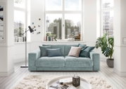 Zweiersofa in einem hellen Wohnzimmer mit großen Fenstern, dekoriert mit Kissen in verschiedenen Blautönen, aus der Frontalperspektive.