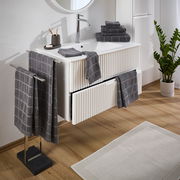 Badezimmer mit grauem Frottierset, bestehend aus Handtüchern mit Karomuster, auf einem weißen Waschtisch und Handtuchhalter. Perspektive von schräg oben.