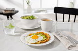 Frühstücksteller mit Waffel, Spiegelei und Avocado, daneben eine Tasse Kaffee, ein Glas Wasser mit Minze und ein Salat in einer Schüssel, aus der Perspektive von schräg oben fotografiert.