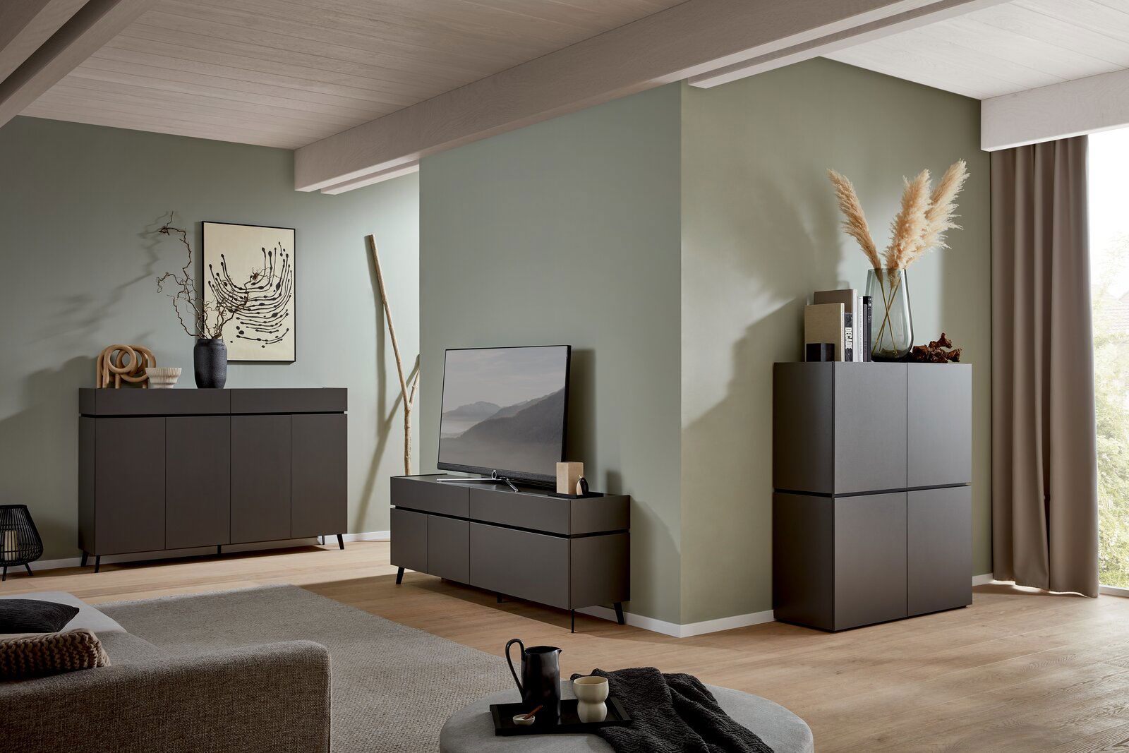 Modernes Wohnzimmer mit einem dunklen Sideboard, einem TV-Lowboard und einem hohen Schrank, dekoriert mit Vasen und Kunstwerken, seitliche Perspektive.