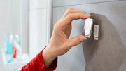 Nahaufnahme einer Hand, die einen tesa Powerstrip Waterproof Haken an einer Badezimmerwand anbringt.