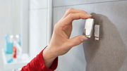 Nahaufnahme einer Hand, die einen tesa Powerstrip Waterproof Haken an einer Badezimmerwand anbringt.