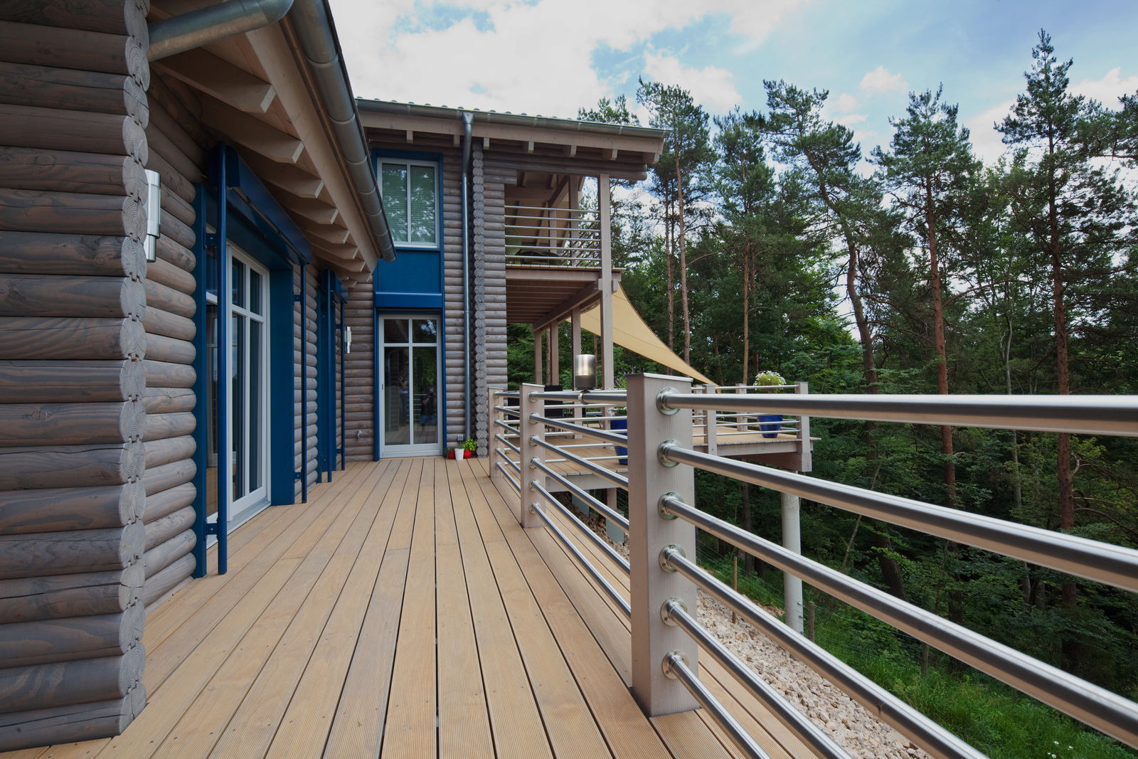 Blick auf ein modernes Holzhaus mit Balkon und Geländer, umgeben von Wald.