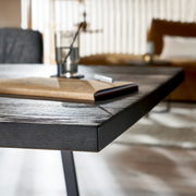 Nahaufnahme eines Esstisches aus dunklem Holz mit Metallbeinen, im Hintergrund unscharf ein Wohnzimmer zu sehen.