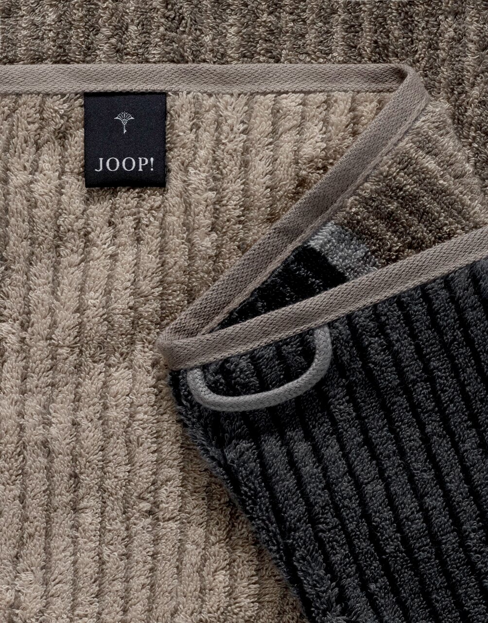 Close-up van een gestreepte gastendoek in verschillende grijstinten met een Joop-label.