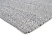 Nahaufnahme eines handgewebten Teppichs in Grautönen, perspektivisch von der Seite aufgenommen.