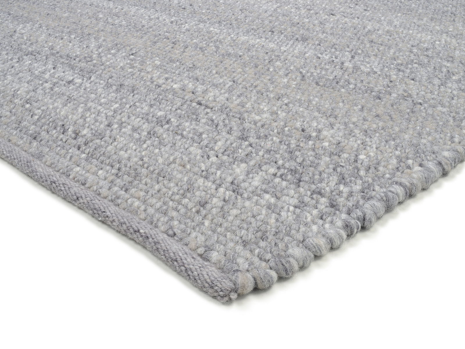 Nahaufnahme eines handgewebten Teppichs in Grautönen, perspektivisch von der Seite aufgenommen.