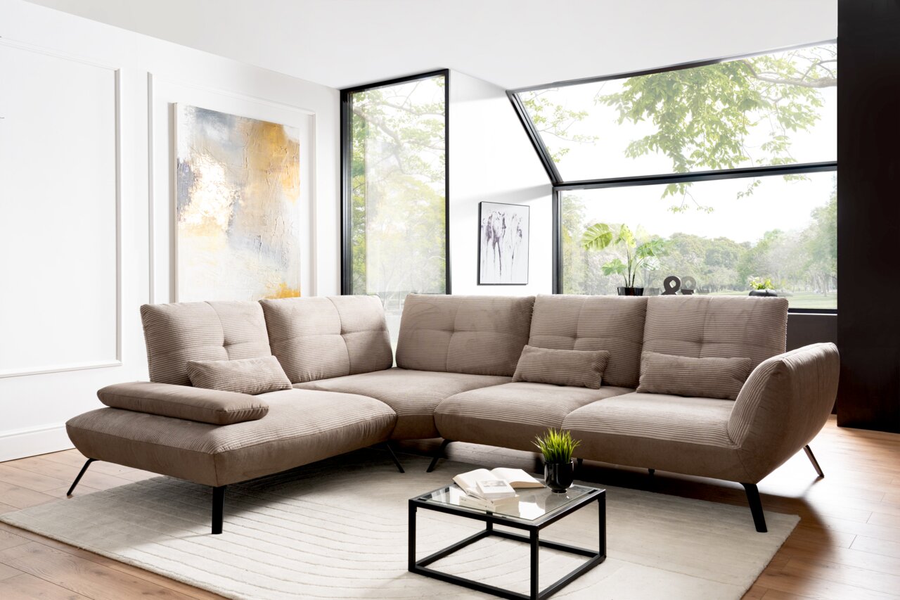 StepOne Ecksofa NEWPORT PLUS Moderne Rundecke in einem hellen Wohnzimmer mit großen Fenstern, die einen Blick ins Grüne bieten. Perspektive von vorne links.