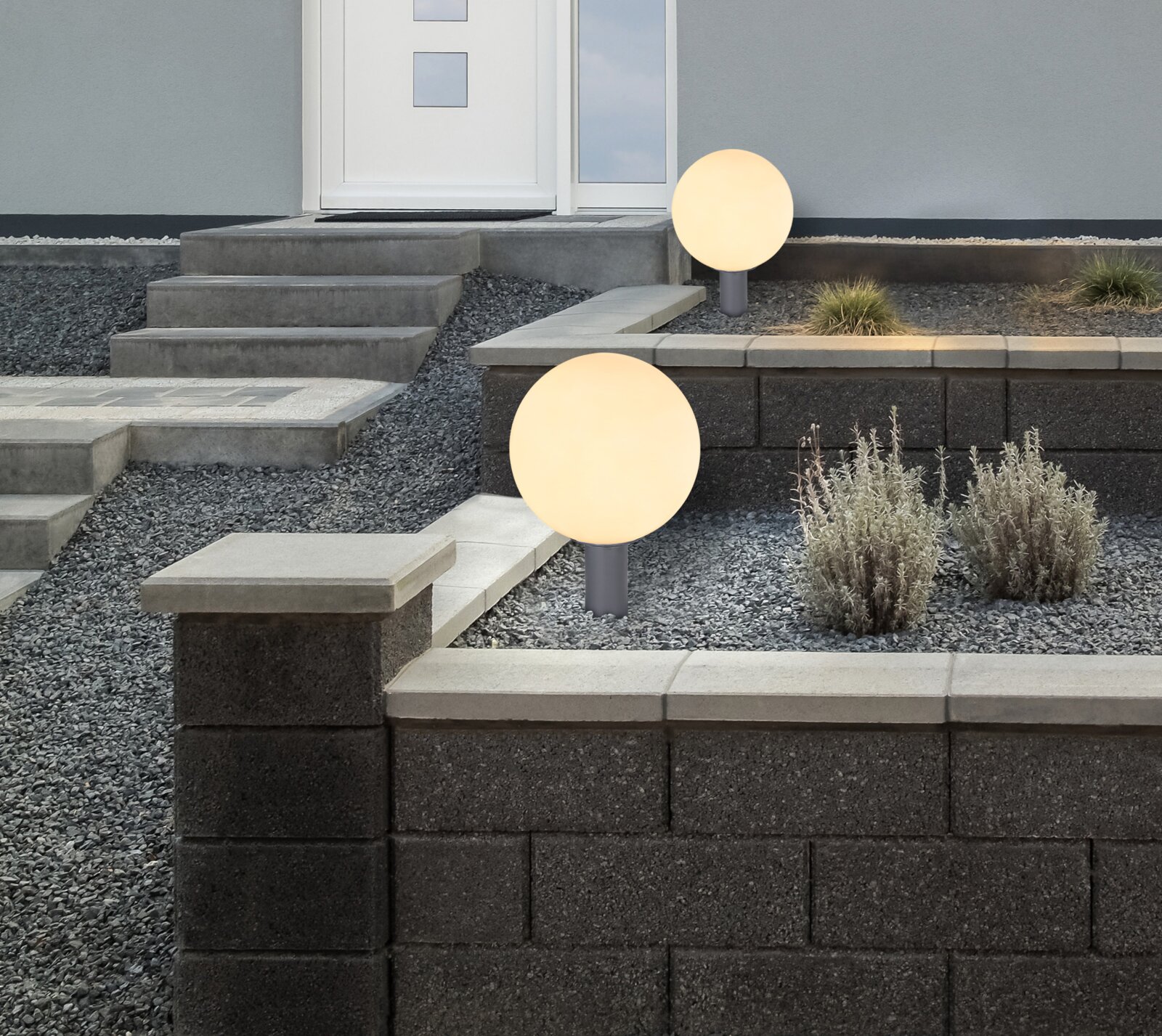 Moderne Außenleuchte in Kugelform, installiert in einem gepflegten Gartenbereich mit Treppen und Pflanzen, seitliche Perspektive.