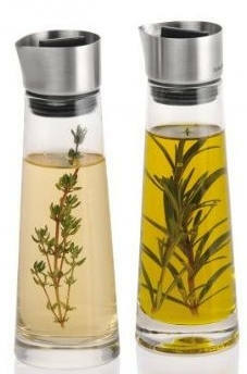 Zwei Glasflaschen mit Edelstahlverschluss, gefüllt mit Essig und Öl, jeweils mit Kräutern, aus frontaler Perspektive.