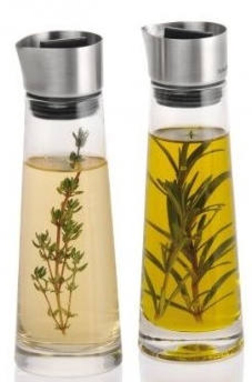 Zwei Glasflaschen mit Edelstahlverschluss, gefüllt mit Essig und Öl, jeweils mit Kräutern, aus frontaler Perspektive.