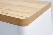 Nahaufnahme einer Schreibtischecke mit abgerundeter Holzkante und weißem Korpus, Perspektive von oben.