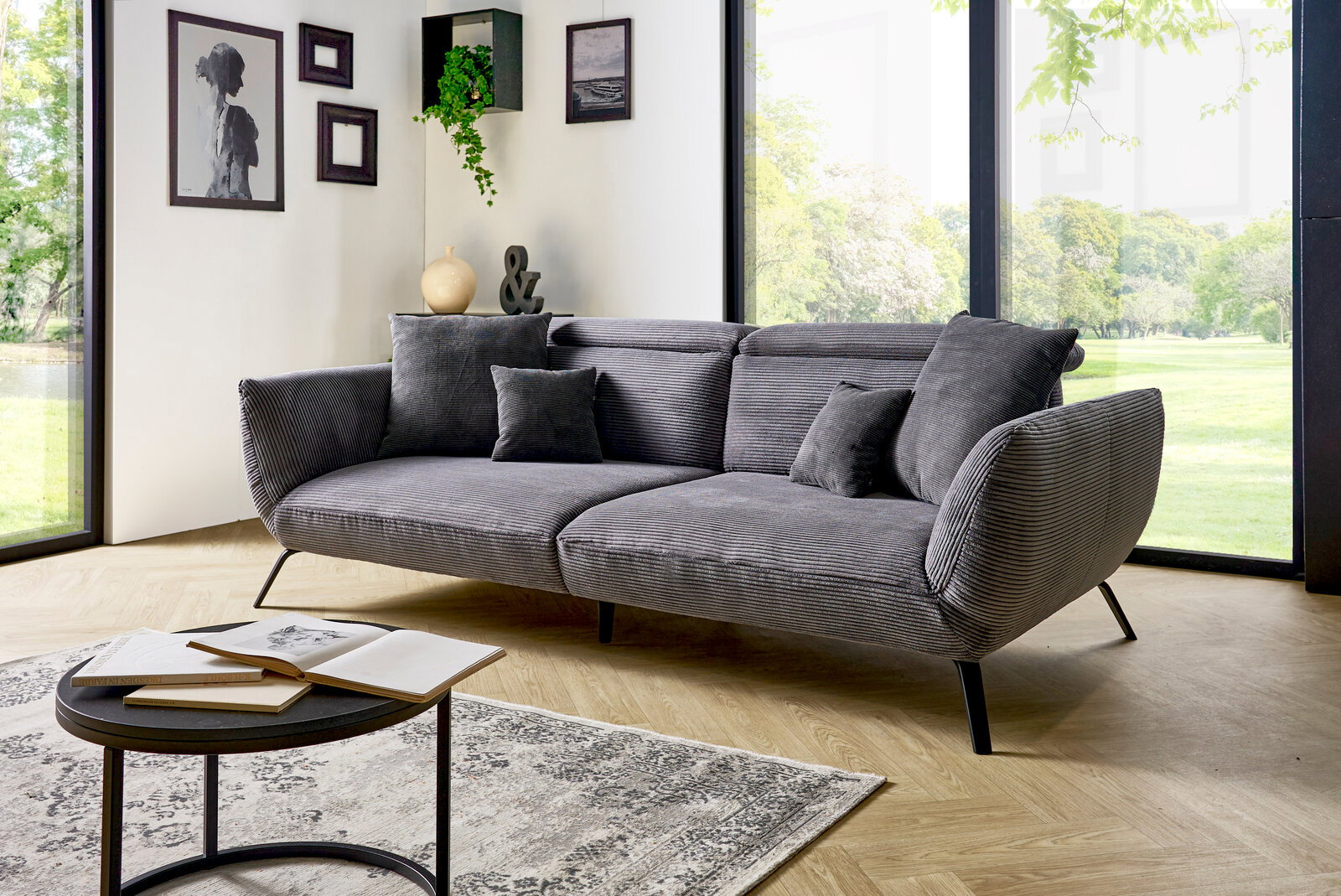 Graues Megasofa in einem modernen Wohnzimmer mit großen Fenstern, seitliche Perspektive