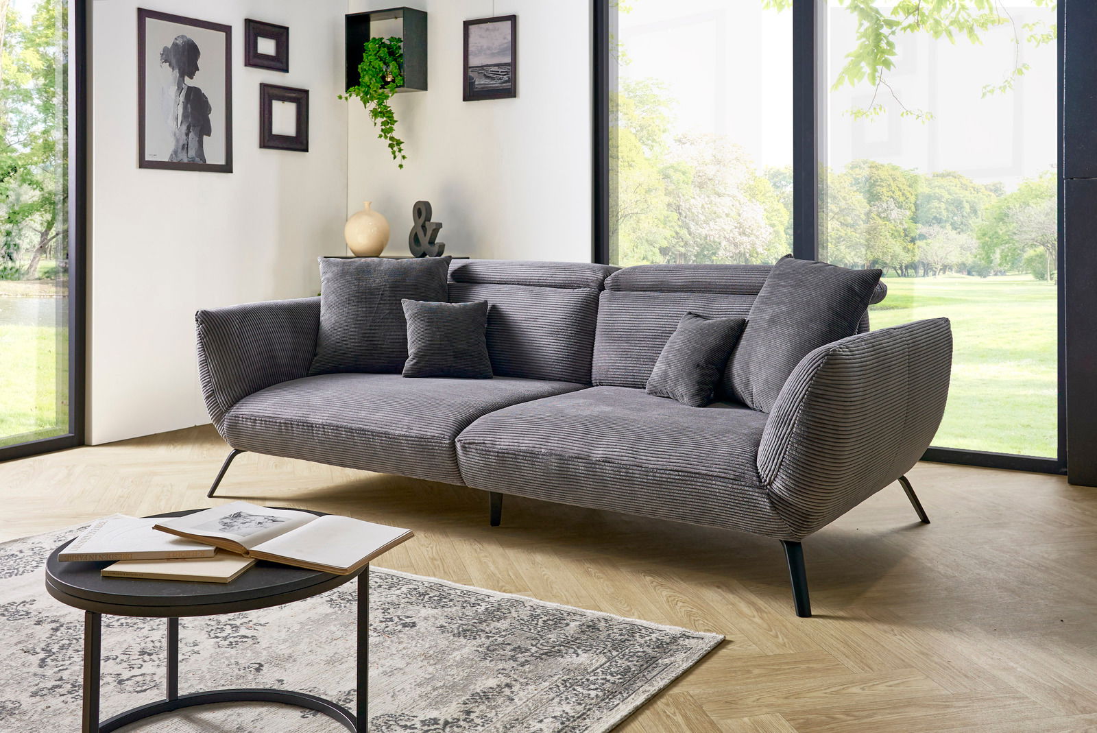 Graues Megasofa in einem modernen Wohnzimmer mit großen Fenstern, seitliche Perspektive