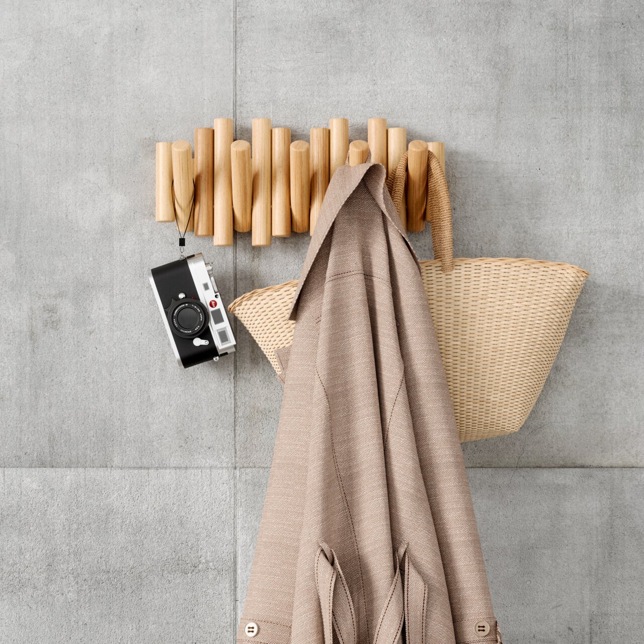 Wandgarderobe aus Holz mit mehreren Haken, an der eine Kamera, ein Mantel und eine Tasche hängen. Ansicht von vorne.