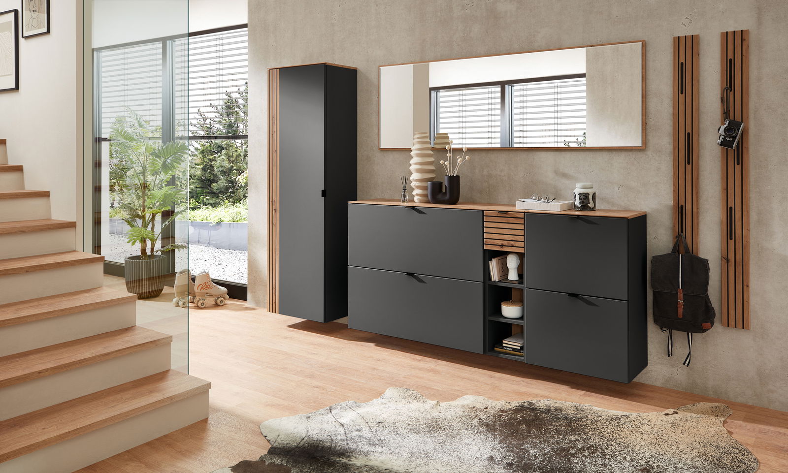 Garderoben-Set in Graphit mit modernem Design, bestehend aus einem hohen Schrank, einer Kommode mit Schubladen und offenen Fächern, einem großen Spiegel und Wandpaneelen mit Haken. Perspektive: Frontalansicht in einem hellen, modernen Flur.