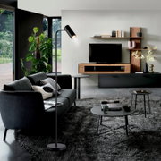 Modernes Wohnzimmer mit schwarzem Sofa, Stehlampe und TV-Wandmöbel aus Holz/Schwarz mit Regalen; Perspektive: frontale Raumansicht leicht von links.