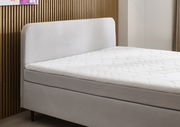 Seitliche Ansicht eines modernen Boxspringbetts mit gepolstertem Kopfteil und weißer Matratze vor einer Holzwand.
