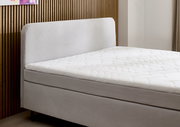 Seitliche Ansicht eines modernen Boxspringbetts mit gepolstertem Kopfteil und weißer Matratze vor einer Holzwand.