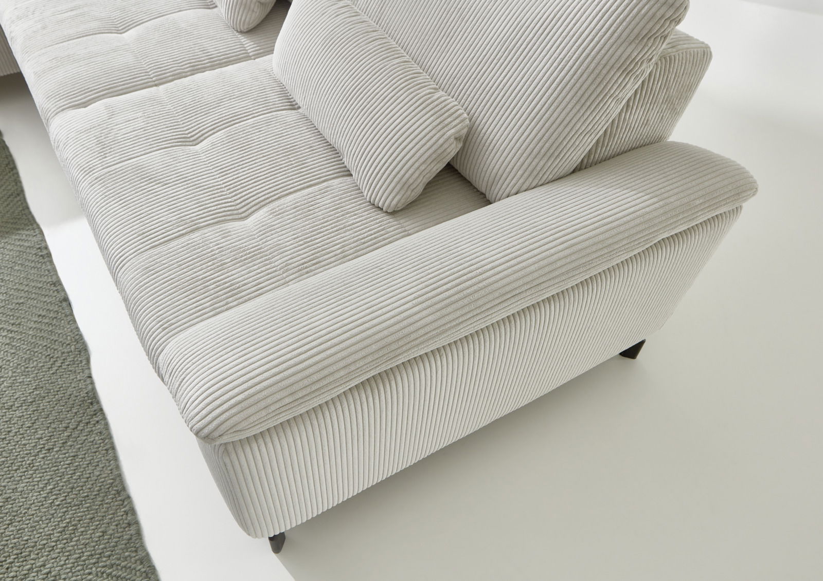 Nahaufnahme eines modernen Ecksofas mit hellgrauem, geripptem Stoffbezug. Die Perspektive zeigt die Armlehne und Sitzfläche von oben.