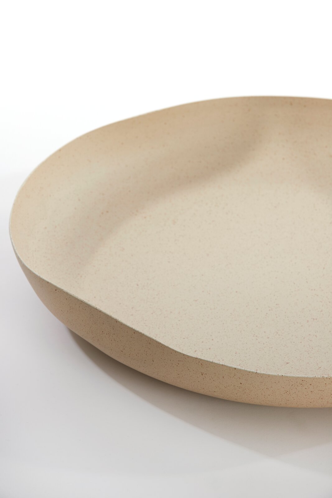 Close-up vanuit schuin bovenaanzicht van een ondiepe, ronde schaal in gespikkeld beige op een witte achtergrond