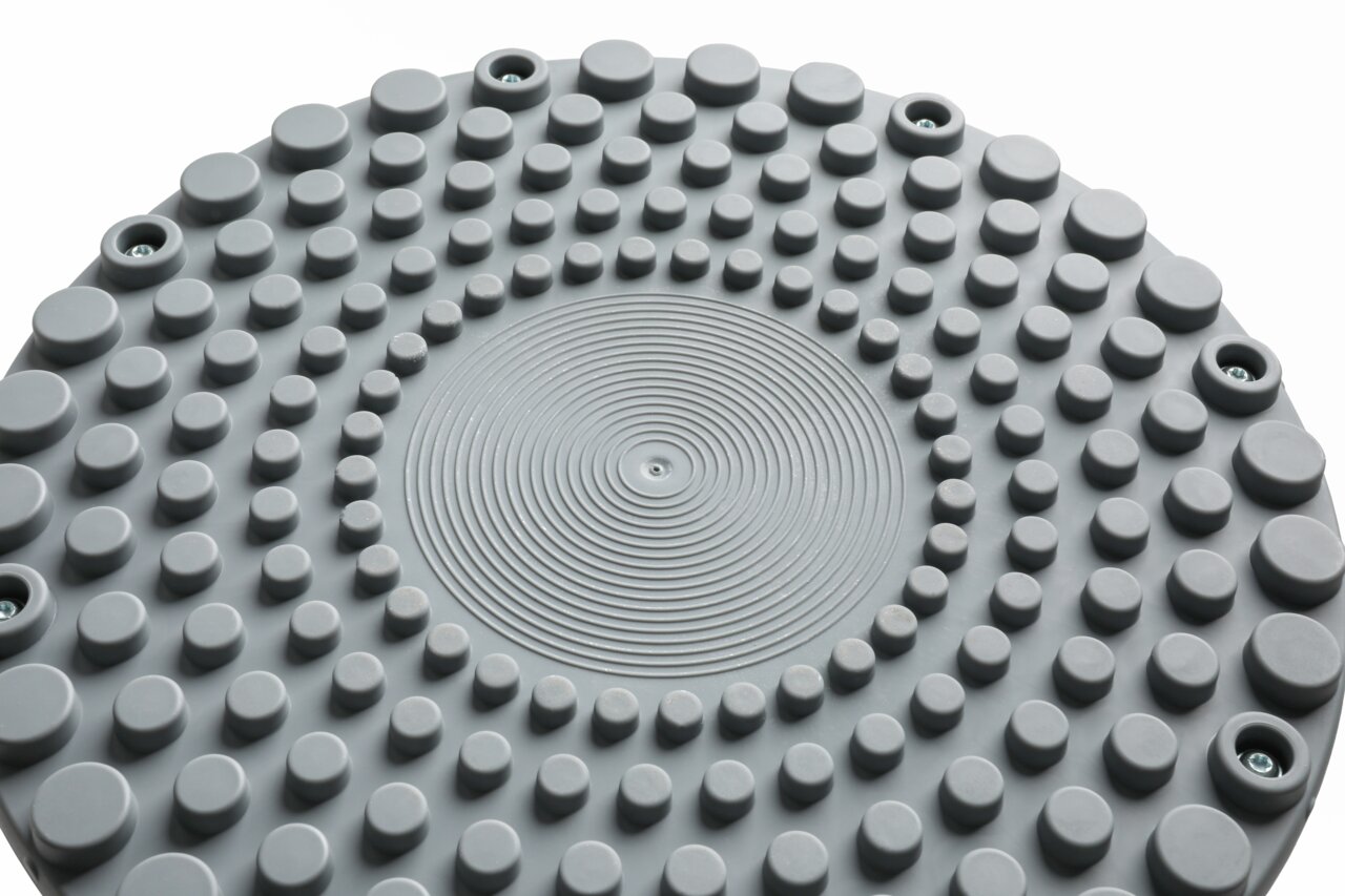 Nahaufnahme der Oberseite eines grauen Schwinghockers mit kreisförmigen Erhebungen und Schraubenlöchern, von oben betrachtet.
