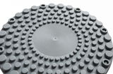 Nahaufnahme der Oberseite eines grauen Schwinghockers mit kreisförmigen Erhebungen und Schraubenlöchern, von oben betrachtet.