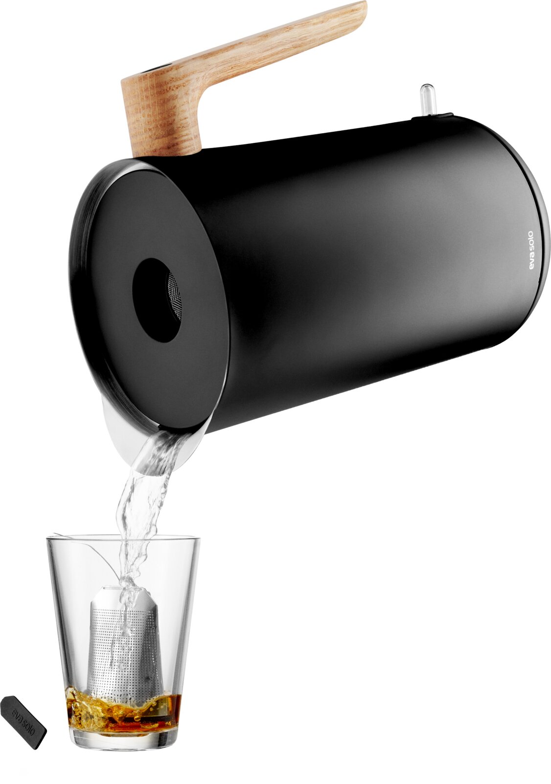 Zwarte cilindervormige theemaker met houten handgreep die vanuit een schuin zijaanzicht thee inschenkt in een glas met metalen infuser