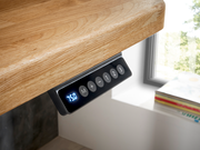Nahaufnahme eines E-Schreibtisch-Bedienfelds unter einer Holzplatte, mit digitaler Anzeige und Tasten zur Höhenverstellung, seitliche Perspektive.