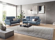 Modernes Wohnzimmer mit zwei blauen Sofas, eines davon ein 2-Sitzer, in einer eleganten, hellen Umgebung mit großen Fenstern und stilvoller Dekoration. Perspektive von vorne.