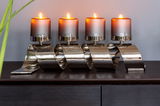 Moderner vierflammiger Kerzenleuchter mit geschwungenem, glänzendem Metallgestell, frontal auf einem dunklen Holztisch präsentiert.