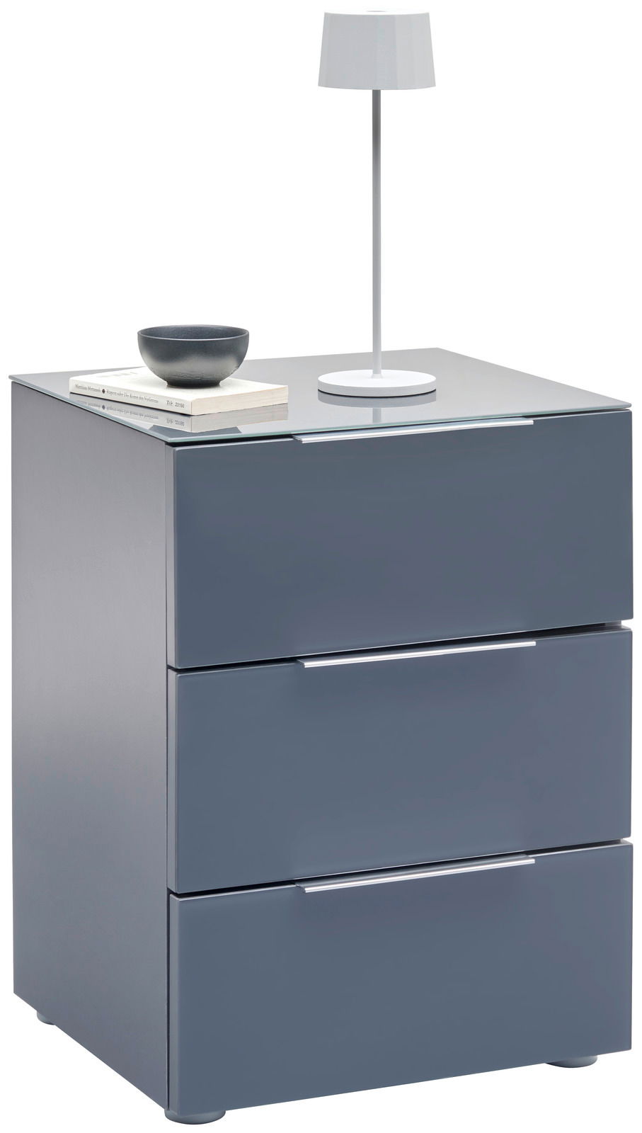 Voleo Nachtkonsole MALIN Moderne Nachtkonsole in Grau mit drei Schubladen, darauf eine weiße Tischlampe und Bücher, seitliche Perspektive