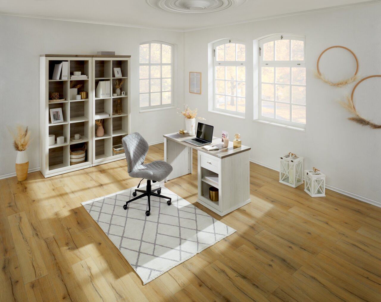 Een licht, modern bureau in een stijlvol ingerichte ruimte met grote ramen, een boekenkast en een ergonomische stoel, gezien vanuit vogelperspectief.