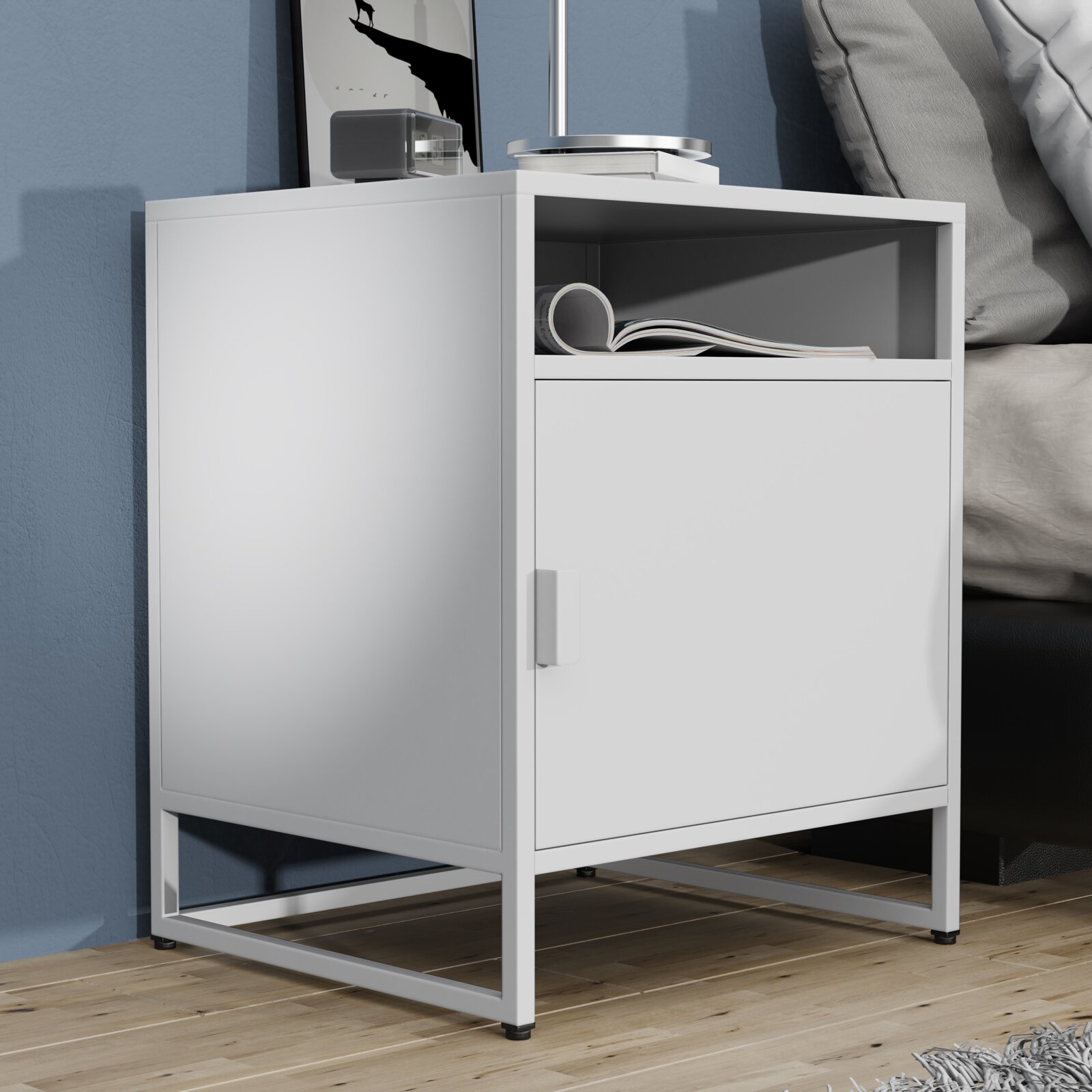 Weißer, moderner Nachttisch/Beistellschrank mit offener Ablage und Türfach auf Metallgestell neben einem Bett, schräg von vorne links fotografiert.