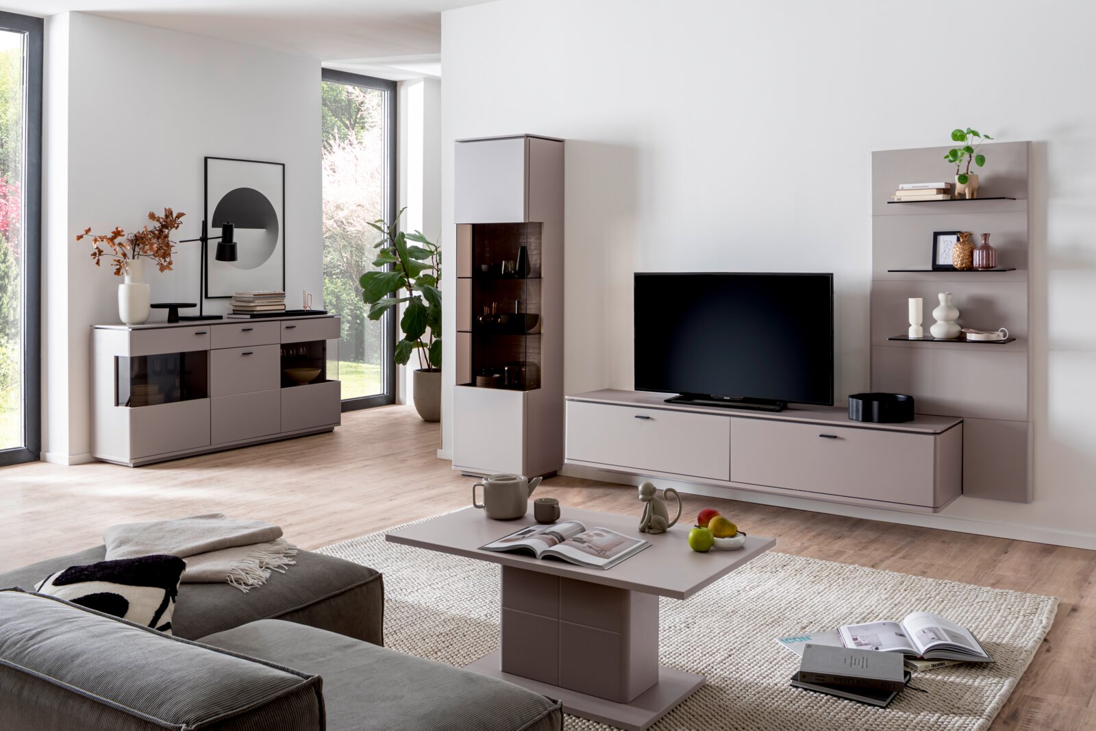 Modernes Wohnzimmer-Setup mit grauer Wohnwand: TV-Lowboard mit Fernseher, Vitrine, Sideboard und Wandregal, aufgenommen in frontaler Perspektive mit leichtem Weitwinkel.