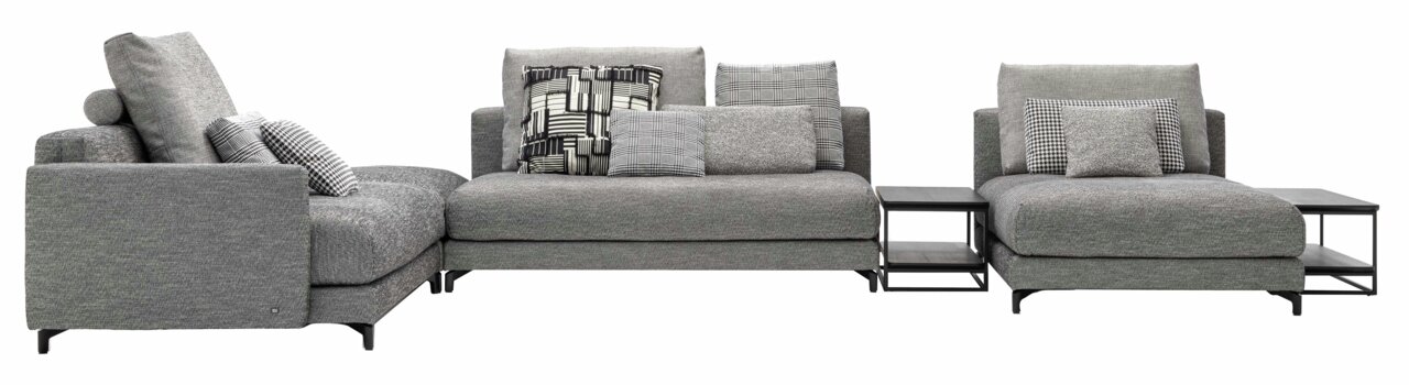 Graue Polsterrundecke mit mehreren Kissen und integrierten Beistelltischen, seitliche Perspektive