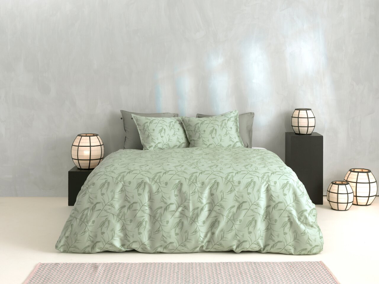 Grüne Bettwäsche mit floralem Muster auf einem Bett, umgeben von modernen Lampen, aus der Frontalperspektive fotografiert.