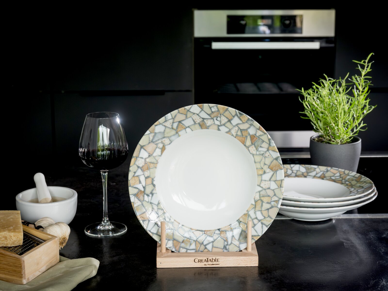 Creatable Pastateller 4-tlg STONE COLLECTION Runder weißer Porzellanteller mit dekorativem Mosaikrand in Beige- und Grautönen auf Holzständer, frontal aus leichter Schrägperspektive in Küchenumgebung fotografiert
