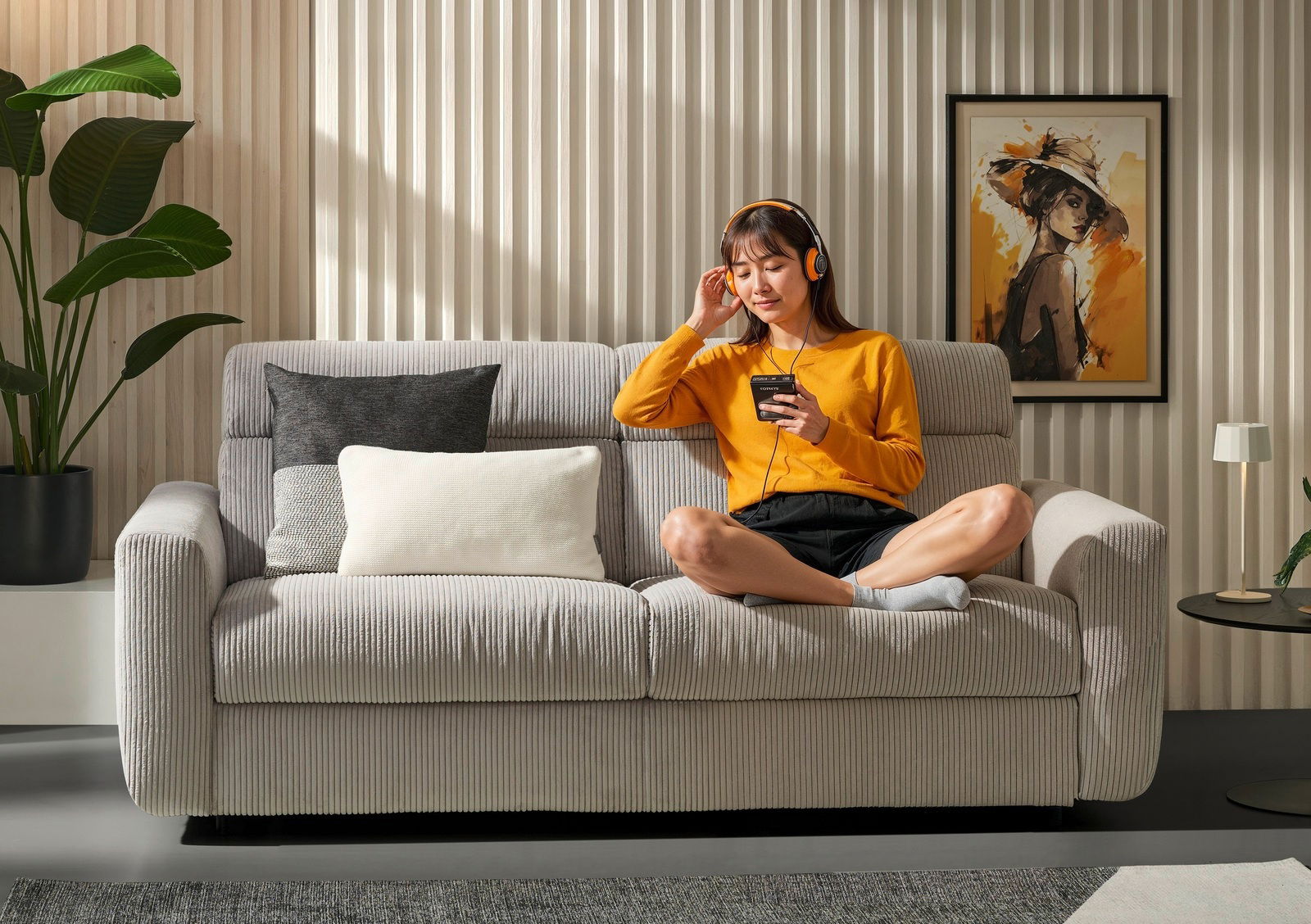 Frau sitzt entspannt auf einem grauen Funktionssofa in einem modernen Wohnzimmer, frontal betrachtet.