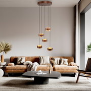 Moderne LED-Hängeleuchte mit mehreren runden Leuchtelementen, hängend über einem stilvollen Wohnzimmer mit braunem Sofa und Couchtisch, seitliche Perspektive.