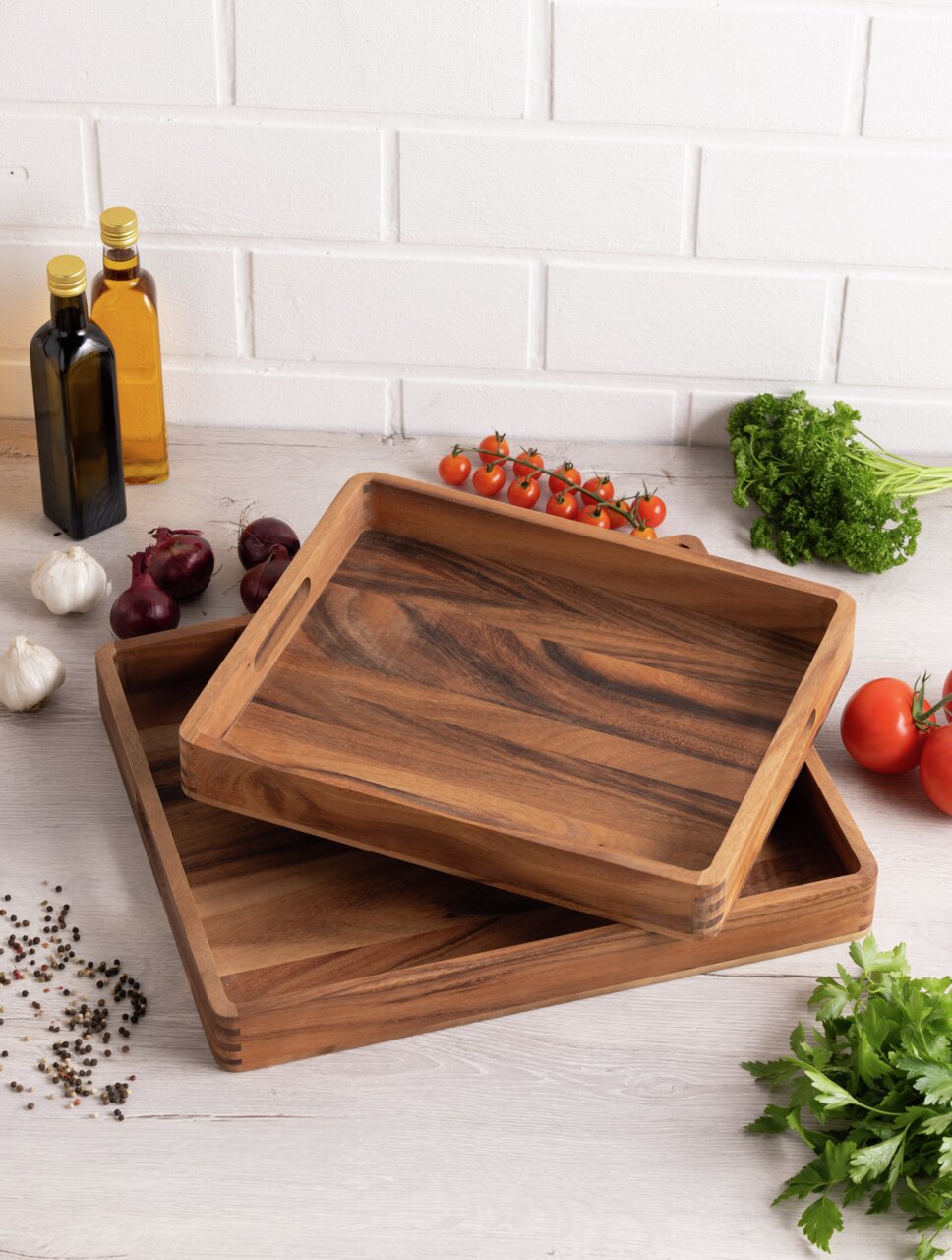 Zwei hölzerne Tabletts in rechteckiger Form, übereinander gestapelt, auf einer Küchenarbeitsplatte mit frischen Zutaten wie Tomaten, Kräutern und Gewürzen. Perspektive von oben.