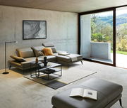 Moderner Wohnraum mit einem eleganten Couchtisch in der Mitte, umgeben von einem stilvollen Sofa und einem großen Fenster mit Blick auf die Natur. Perspektive von vorne.