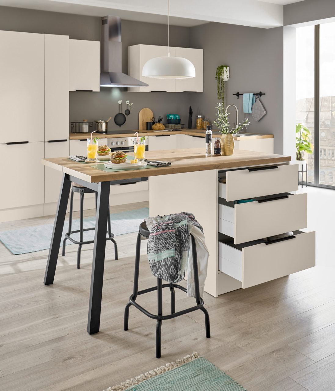 Moderne Küche mit weißer Kücheninsel und Holzarbeitsplatte, drei geöffneten Schubladen, Barhockern und gedecktem Frühstück; Perspektive: frontale, leicht seitliche Ansicht auf die Insel.