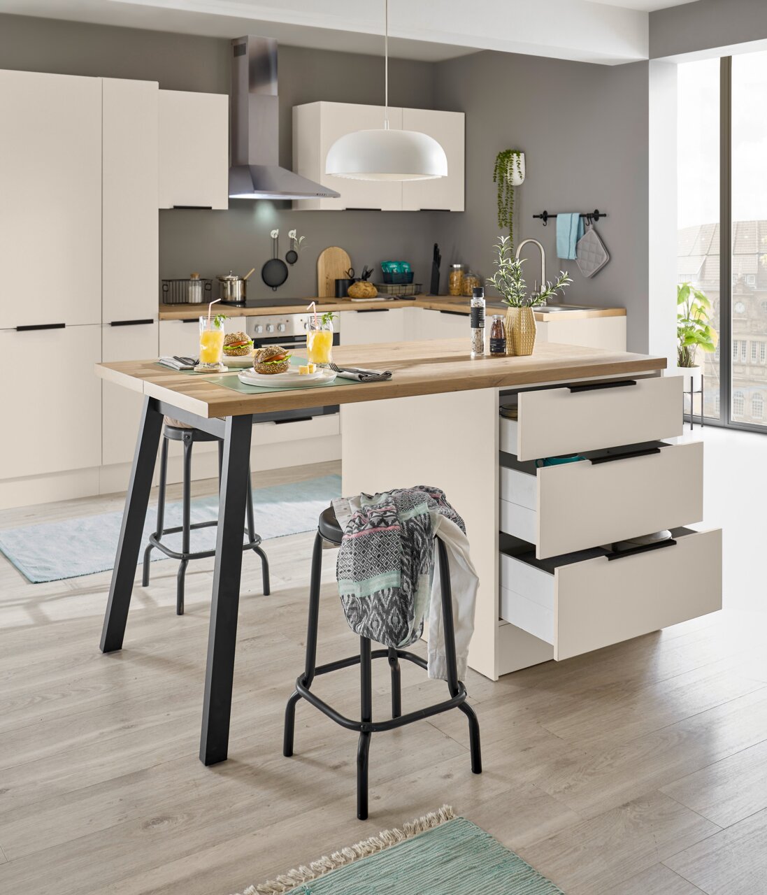 Moderne keuken met een wit kookeiland en een houten werkblad, drie open lades, barkrukken en een gedekte ontbijttafel; perspectief: vooraanzicht, licht zijdelings op het kookeiland.