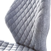 Close-up van een grijze draaistoel met gewatteerde stoffen bekleding, gezien vanaf de zijkant.