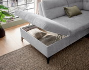 Graues Ecksofa mit Stauraum, geöffnet, von schräg oben fotografiert. Kissen im Stauraum sichtbar.