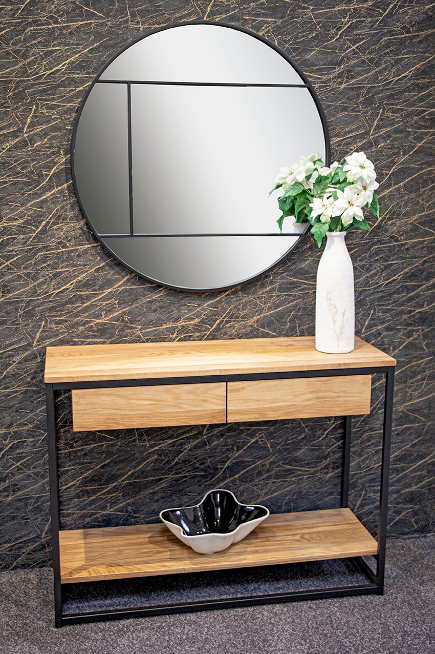 Runder Wandspiegel mit segmentierter Optik über einer Konsole aus hellem Holz mit schwarzem Metallgestell, seitliche Frontansicht; daneben weiße Vase mit Blumen vor dunkler Marmorwand.