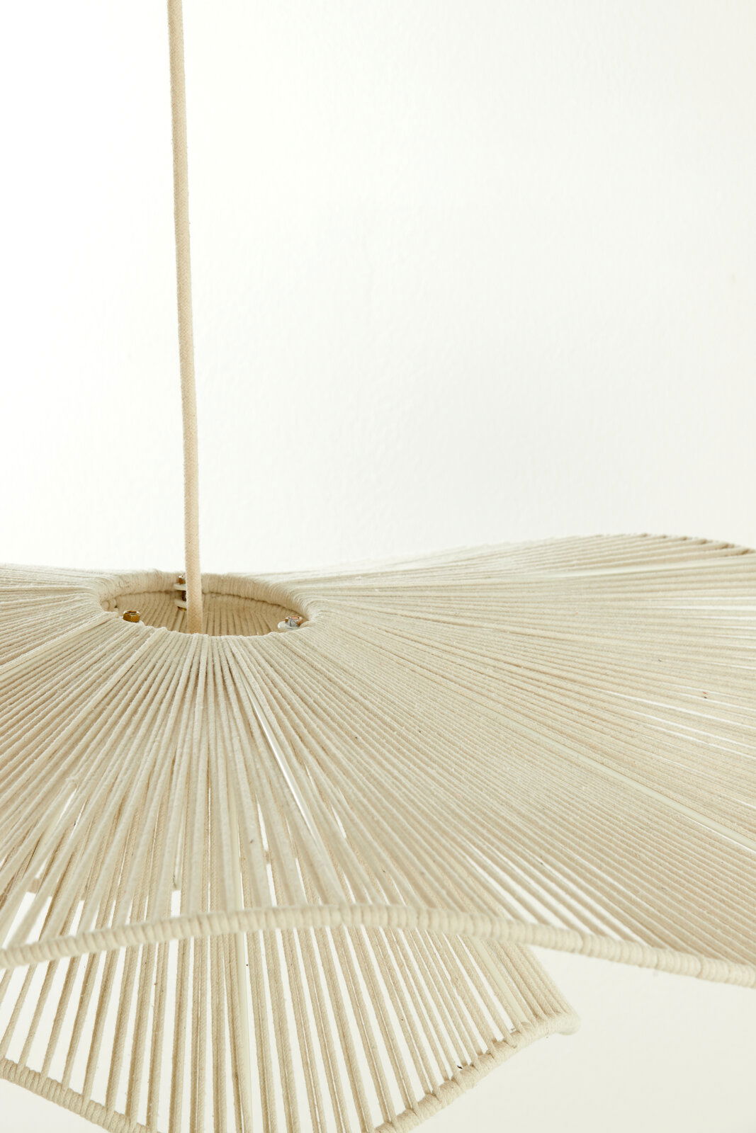 Nahaufnahme einer Hängeleuchte mit einem Schirm aus beigem Stoff, der in Falten gelegt ist. Die Perspektive zeigt die Leuchte von unten.