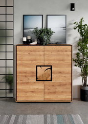 Frontale Ansicht einer modernen Holz-Kommode/Sideboard in Eiche-Optik mit schwarzem Rahmen und quadrativem Griffdetail, dekoriert mit Pflanzen, Kerzen und gerahmten Bildern im Wohnraum.