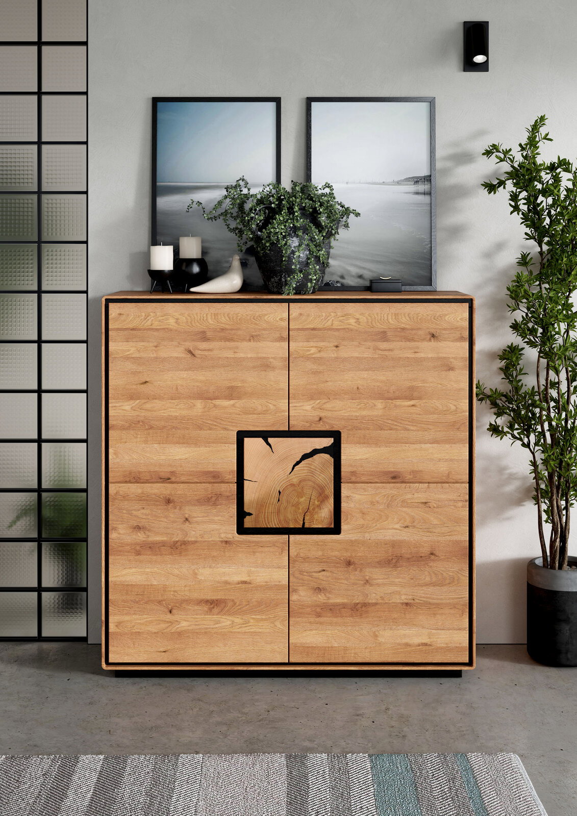 Frontale Ansicht einer modernen Holz-Kommode/Sideboard in Eiche-Optik mit schwarzem Rahmen und quadrativem Griffdetail, dekoriert mit Pflanzen, Kerzen und gerahmten Bildern im Wohnraum.
